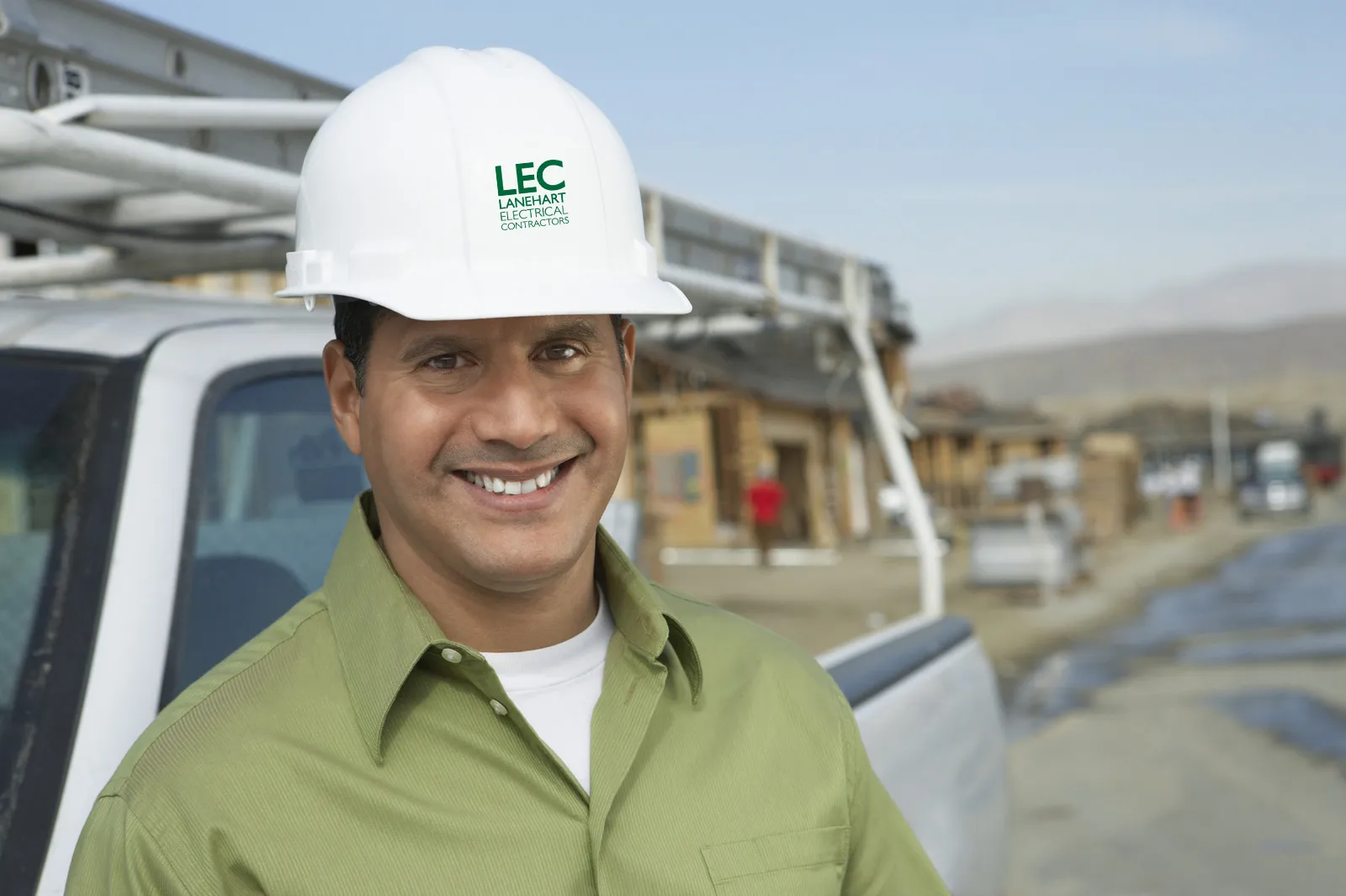 Electrician in an LEC hard hat beside a work truck on a new construction site